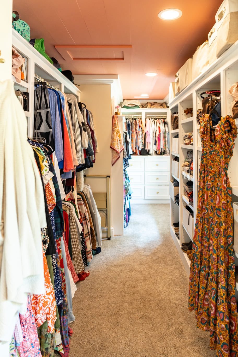 Bright walk-in closet with storage and white custom cabinetry and peach colored ceilings