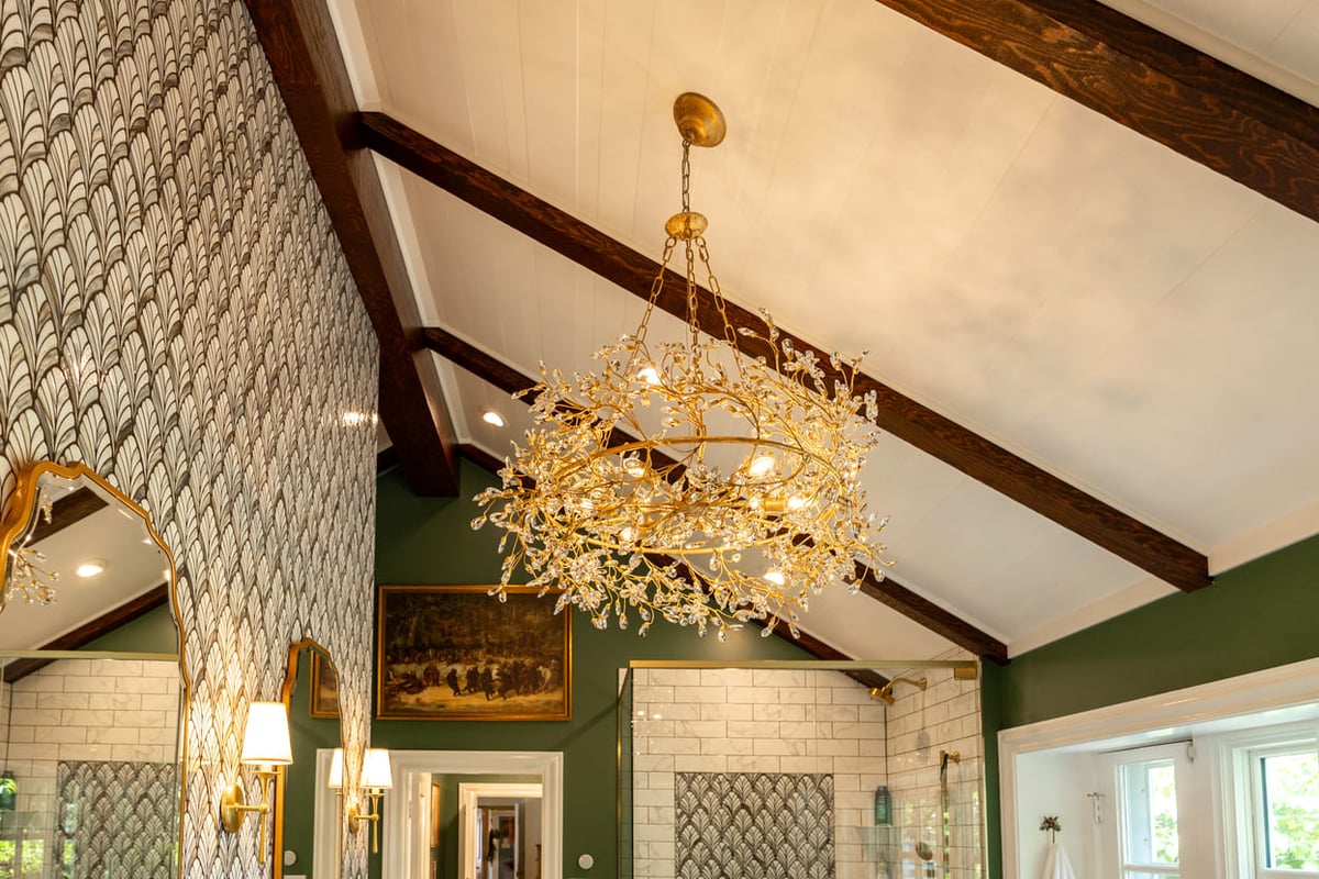 Gold chandelier on vaulted ceilling in bathroom with wallpaper and green painted walls
