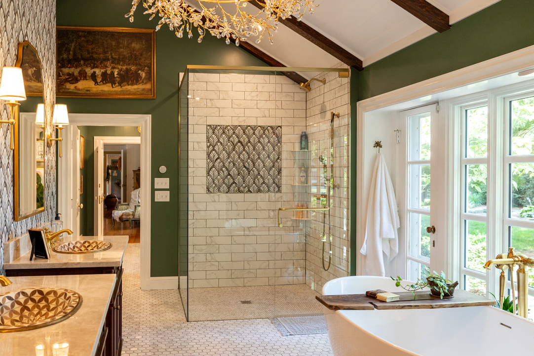 Large glass walkin shower with gold accents, white tub, and two vanietys in bathroom with green walls