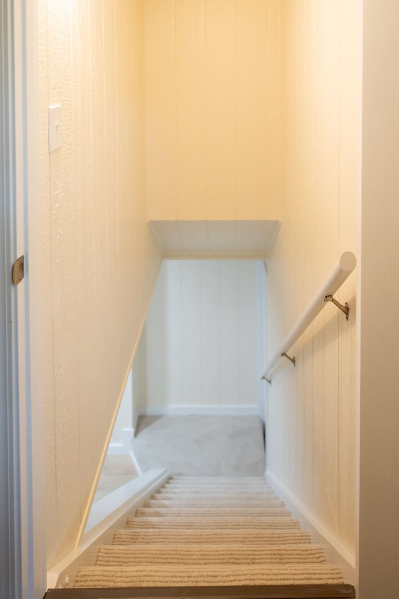 Beige carpet on stairs leading to basement remodel with white walls