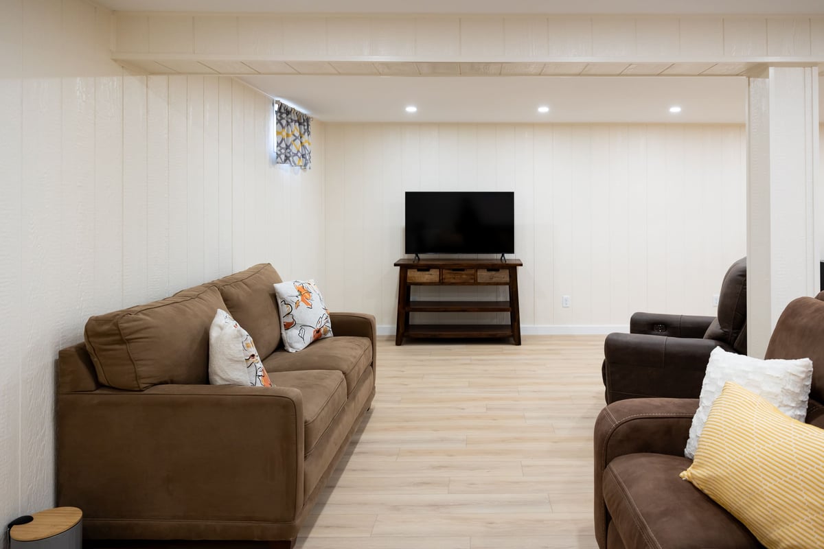 Bown couch & chair with TV in bight white open basement remodel