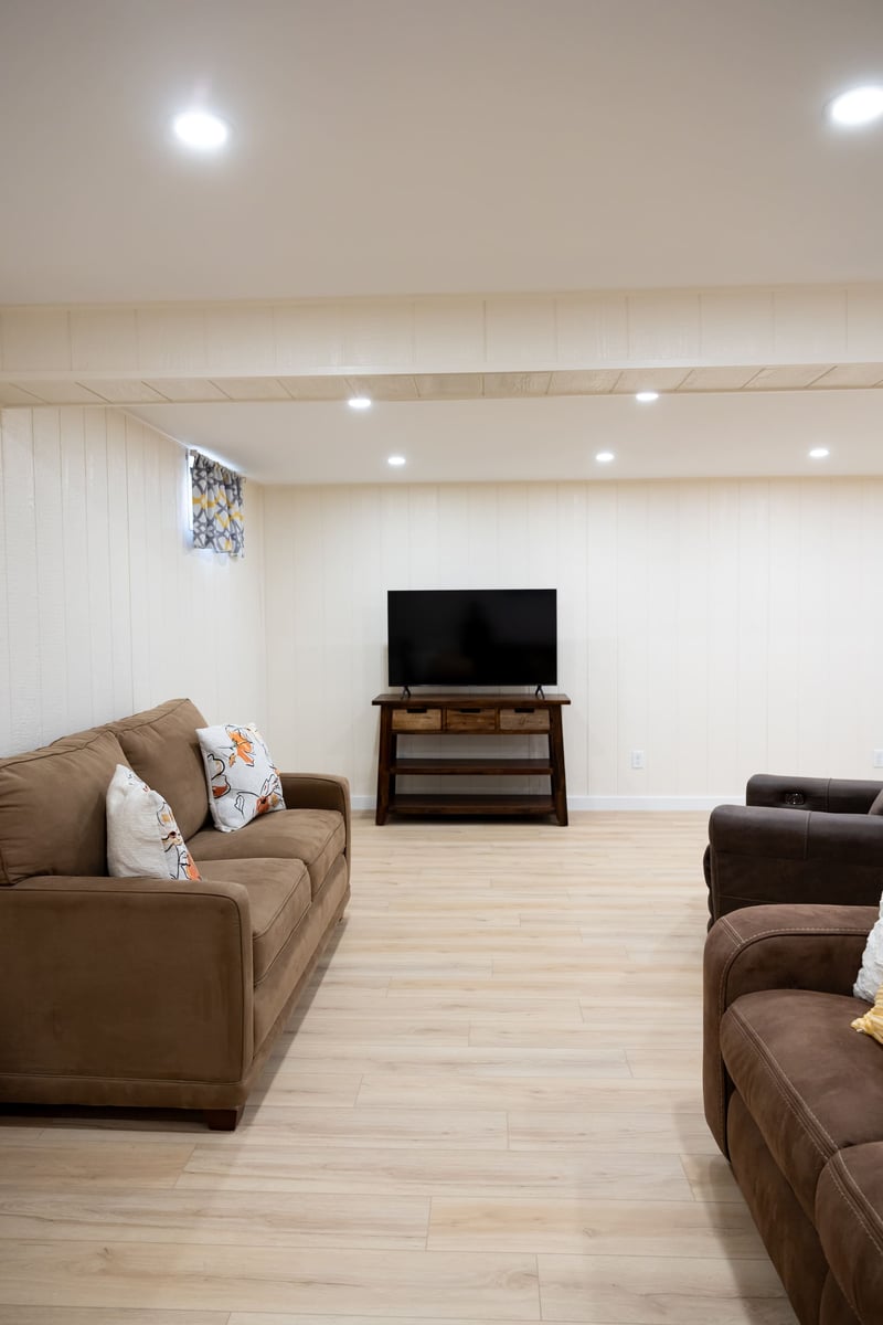Bown couchs & chair with TV in bight white open basement remodel