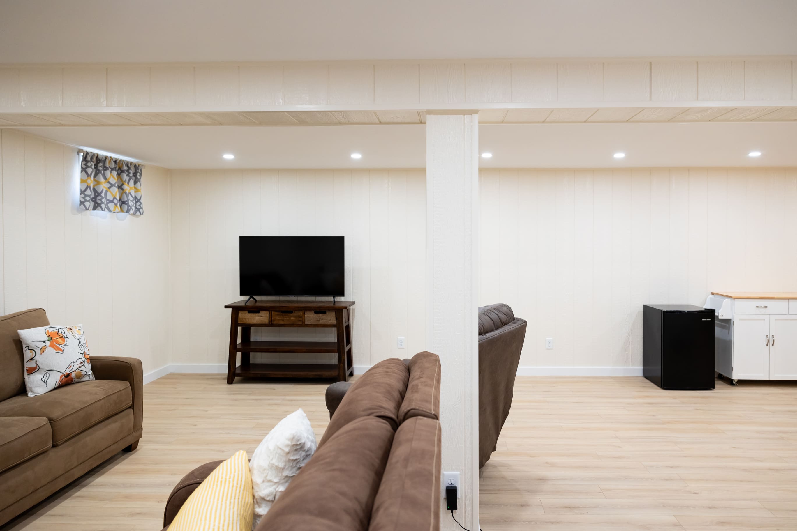Bown couchs & chair with TV, mini fridge, in bight white open basement remodel