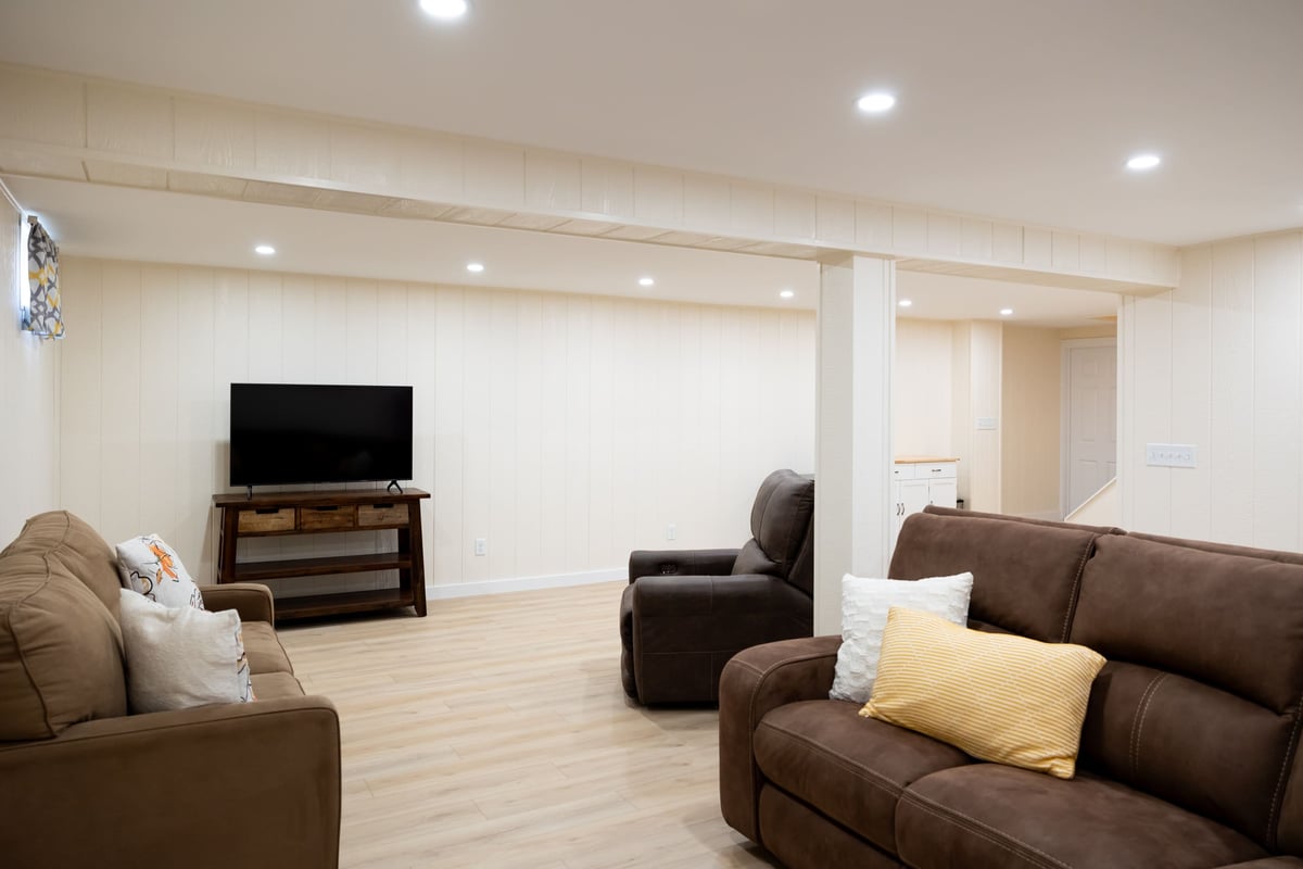 Brown couches, tv on dark wood stand in open white basement remodel