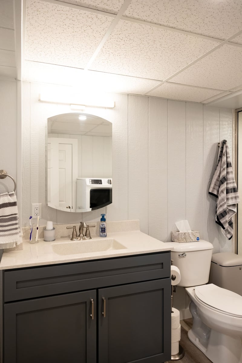 Dark grey vanity with white countertops and white toliet in basement remodel