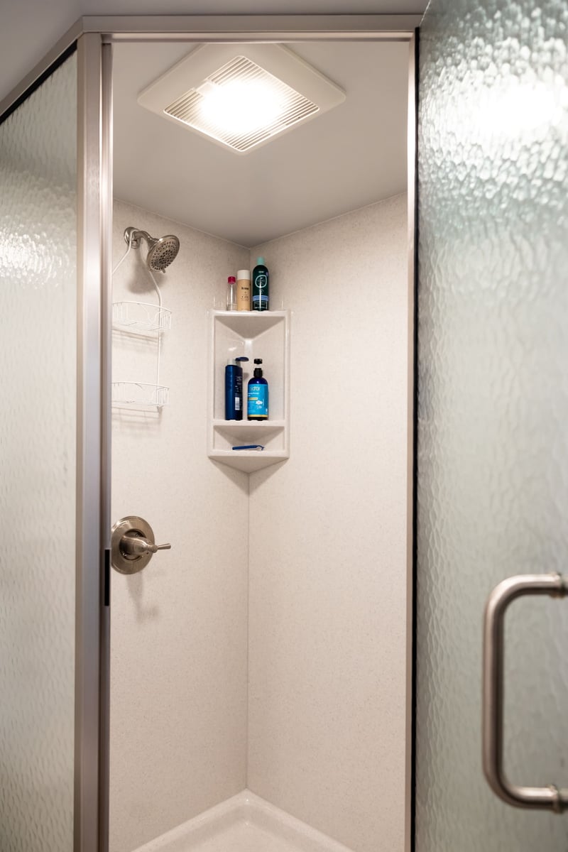 Open door to white shower with built in shelving in basement remodel
