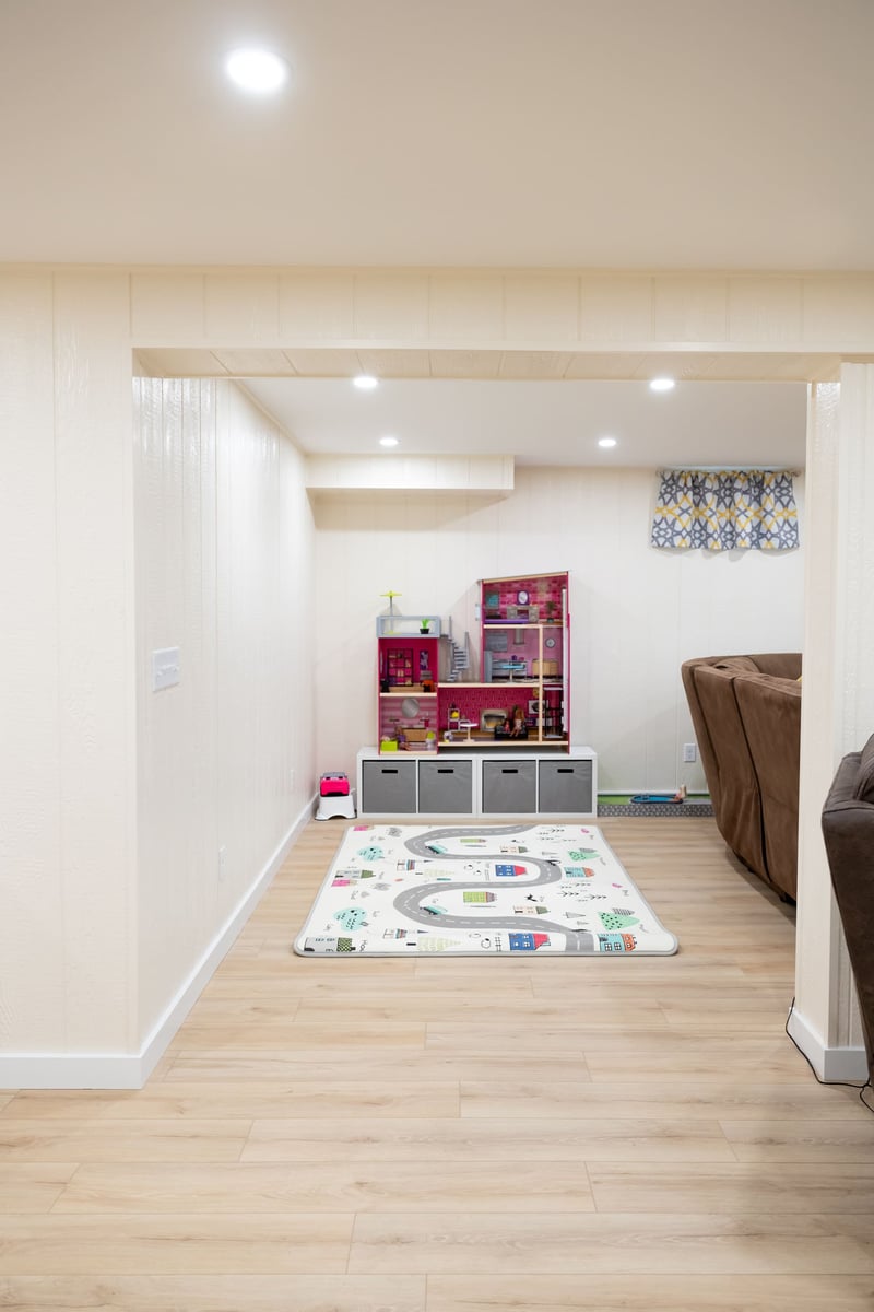 Play area in basement remodel with white walls and light wood floors