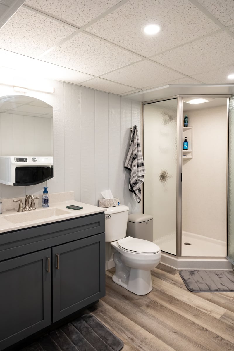 Sink with grey cabinets, white toliet, small shower in basement remodel