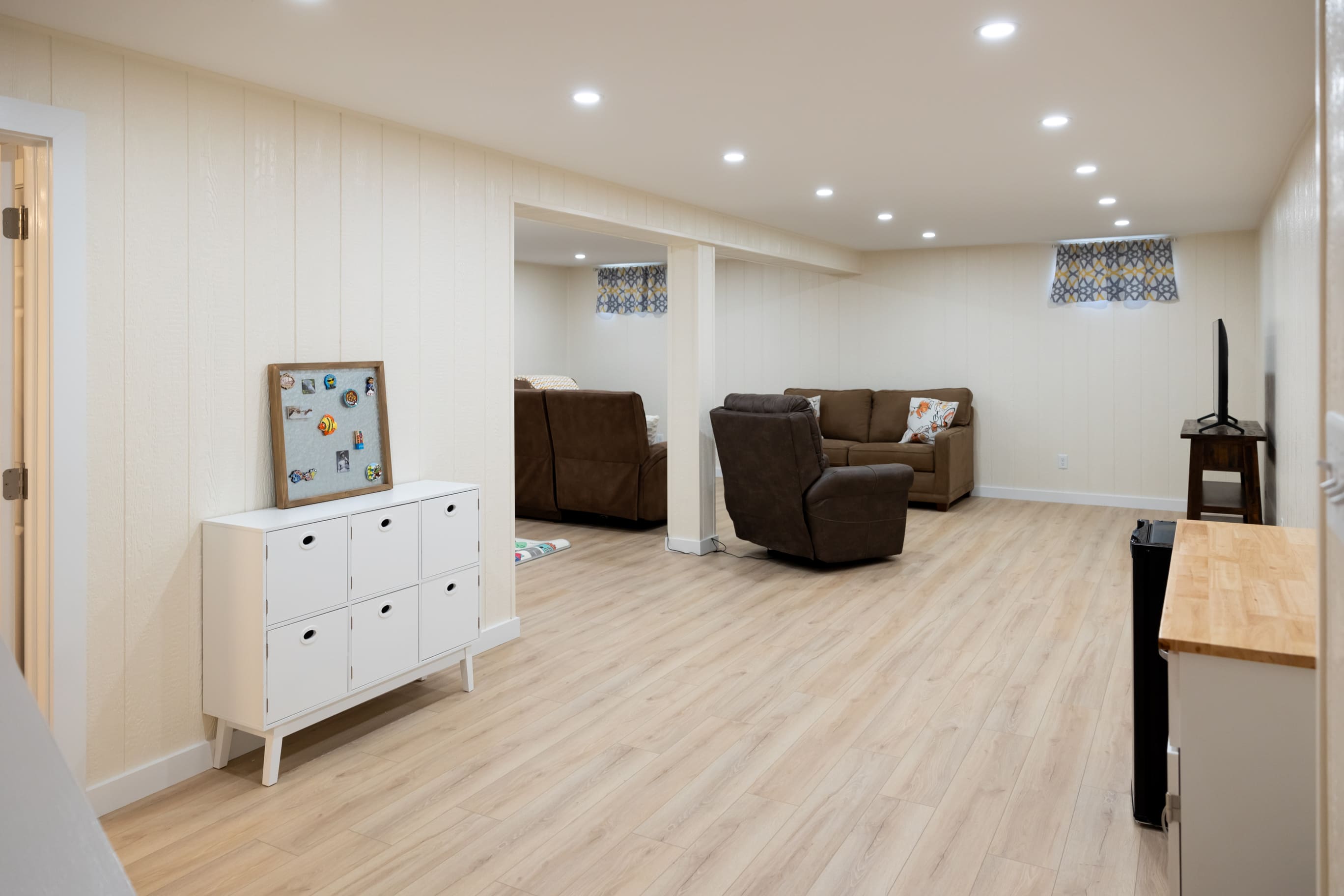 Small storage cabinets in basement remodel with bown couch and light wood floors