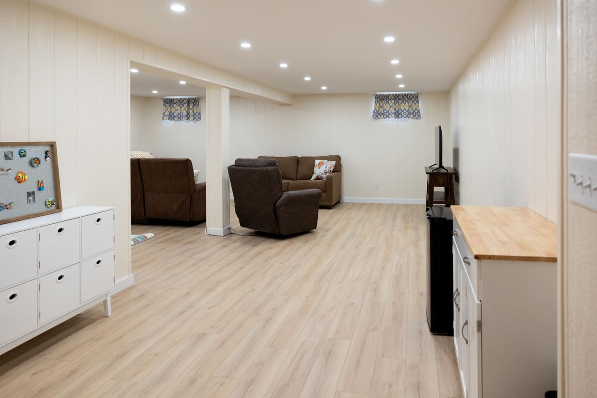 Storage cabinets in well lit basement remodel with bown couch and light wood floors