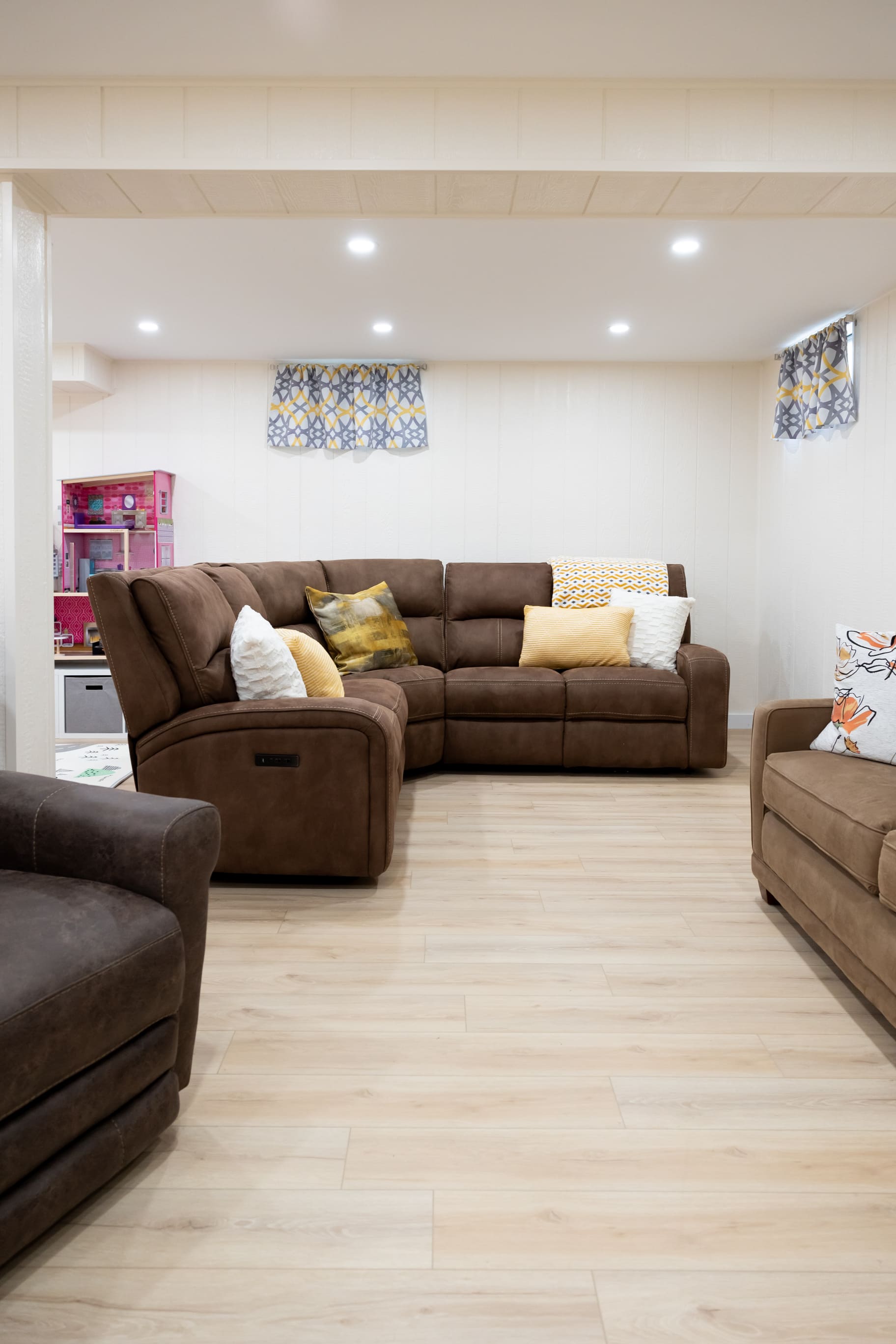 U shaped bown couches and chair in basement remodel with light wood floors