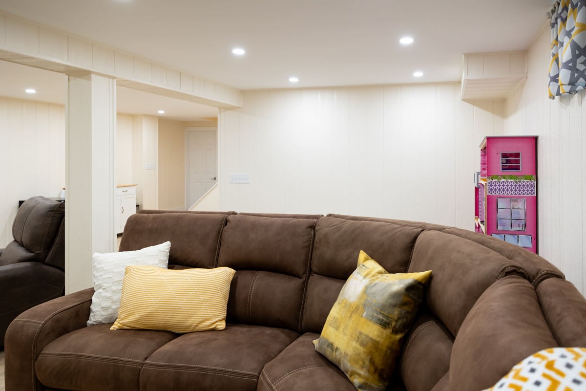 U shaped brown couch with kids play area in basement remodel