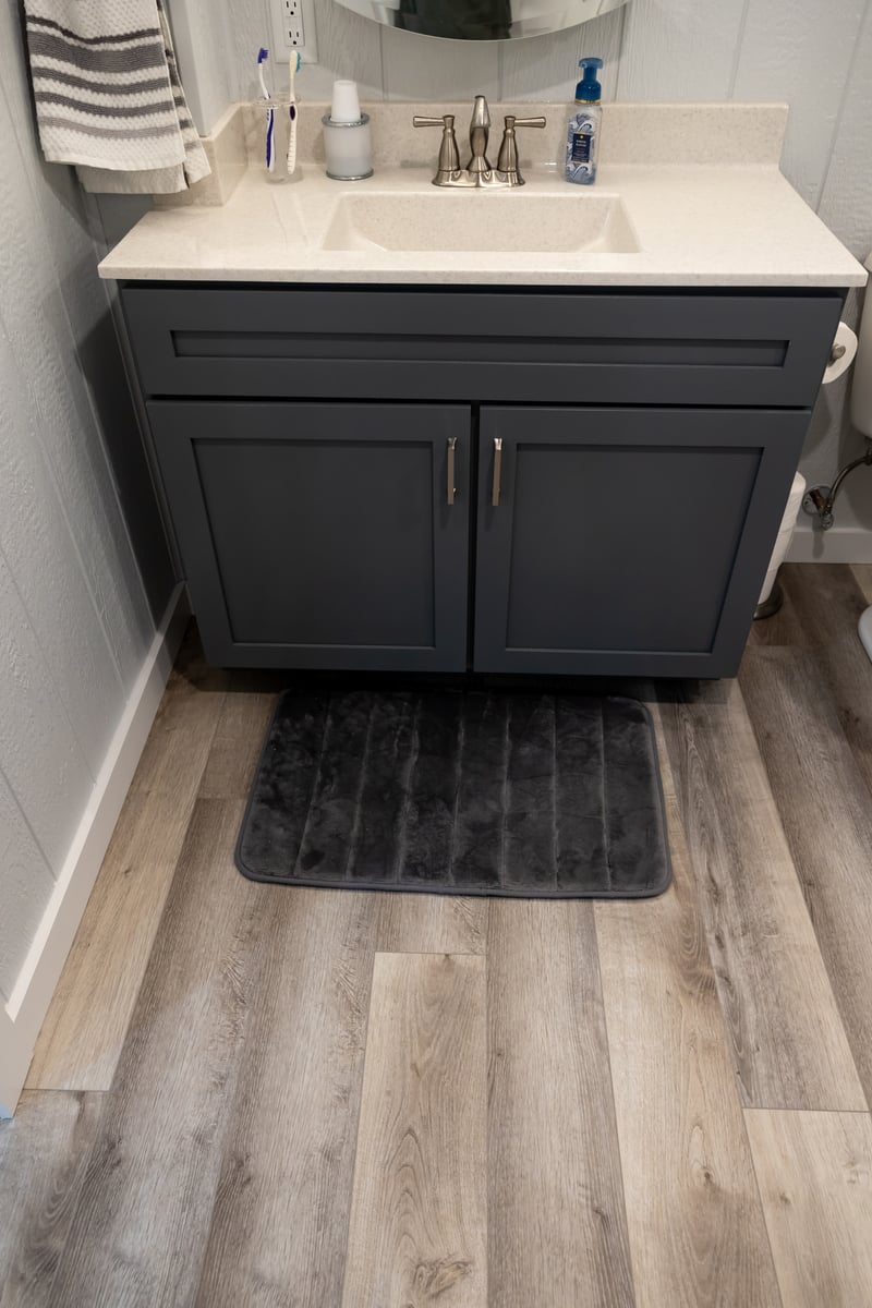 Vaniety with dark grey cabinets and white toliet in basement remodel with light wood floors