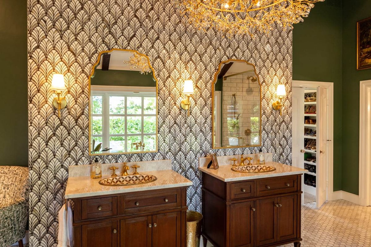 Two Vanietys with gold faucets and dark wood cabinets with green painted walls and wallpaper