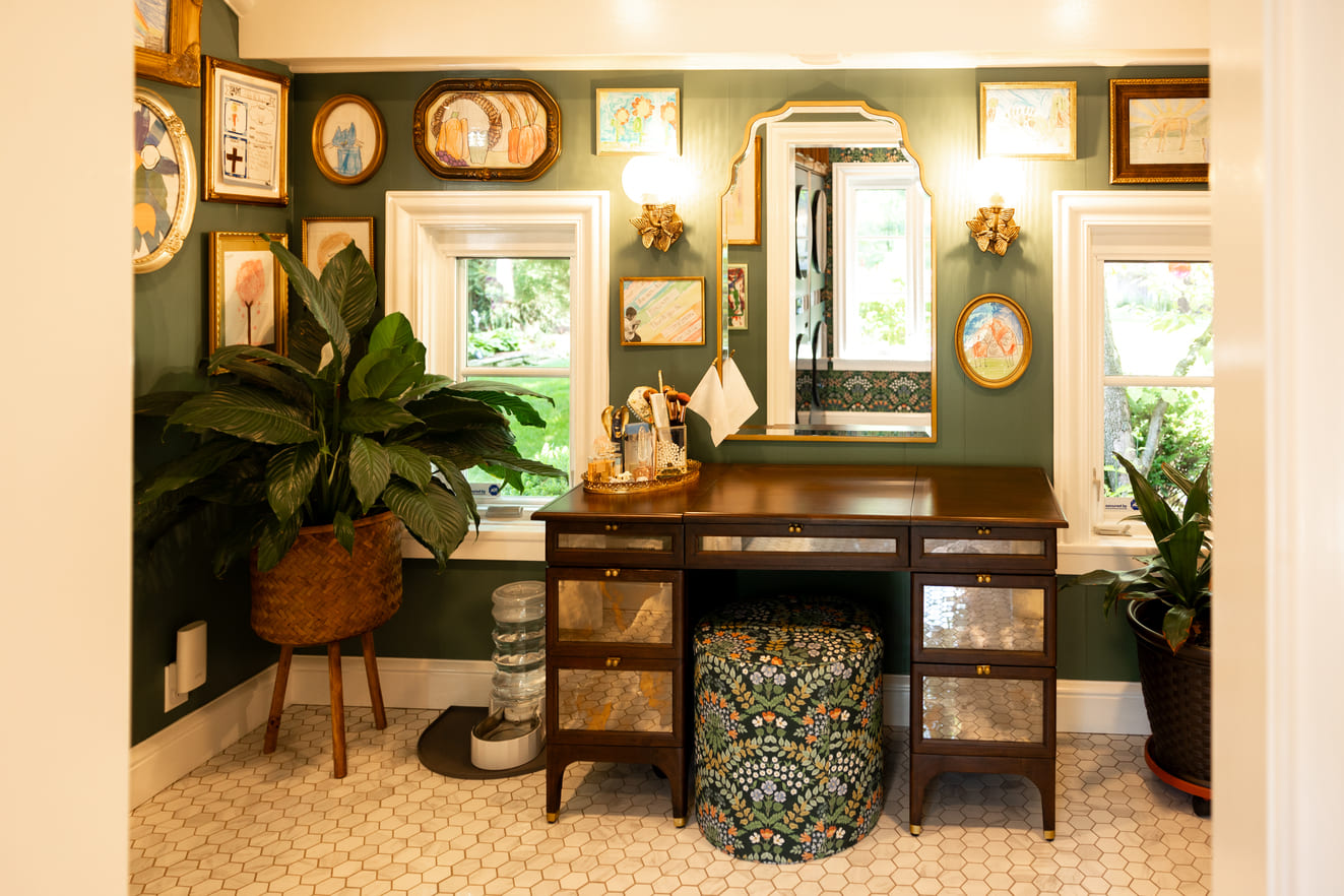 Vaniety area with seat and green walls with hanging artwork 