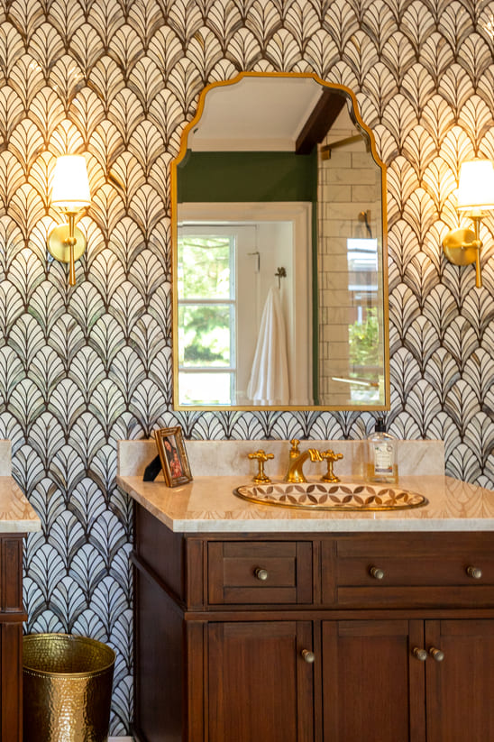 Vanity and sink with gold accents and dark wood cabinetry and wallpaper