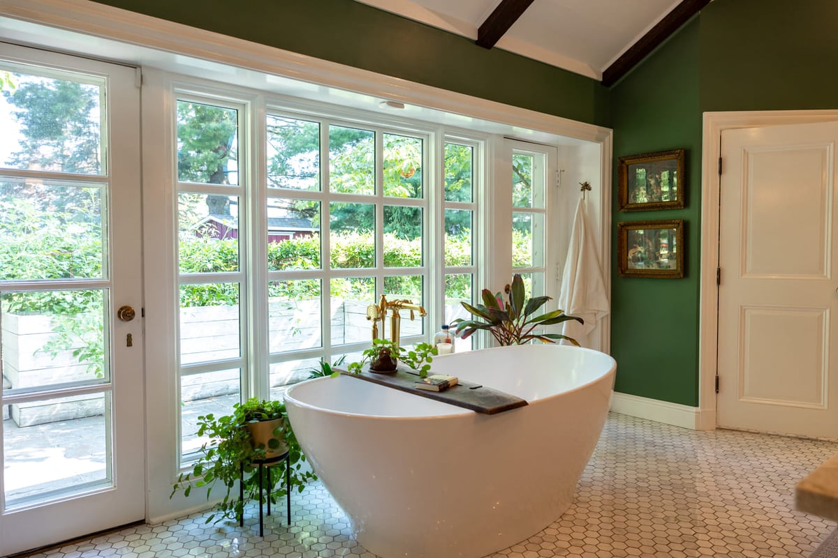 White bathtub infront of windows in bathroom with white tiled floors and green painted walls