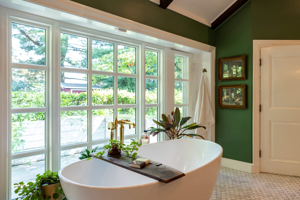 White bathtub with gold fixtures infront of windows in bathroom with green walls 