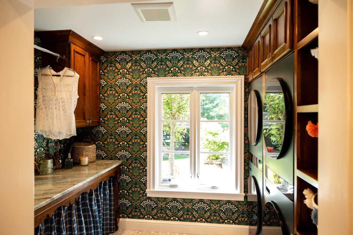 Wood Cabinetry and stone countertop with green,white, and orange wallpaper in laundry room with washer and dryer