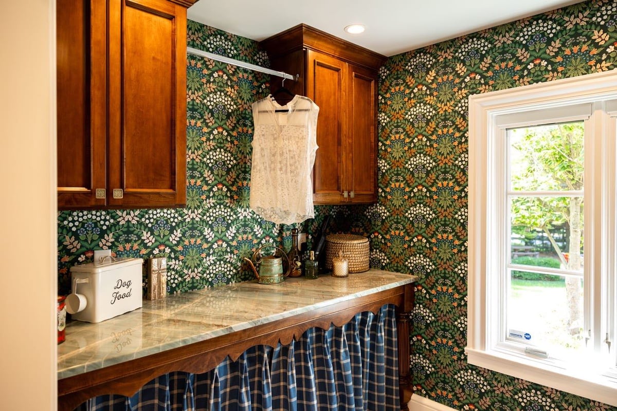 Wood Cabinetry and stone countertop with green,white, and orange wallpaper in laundry room