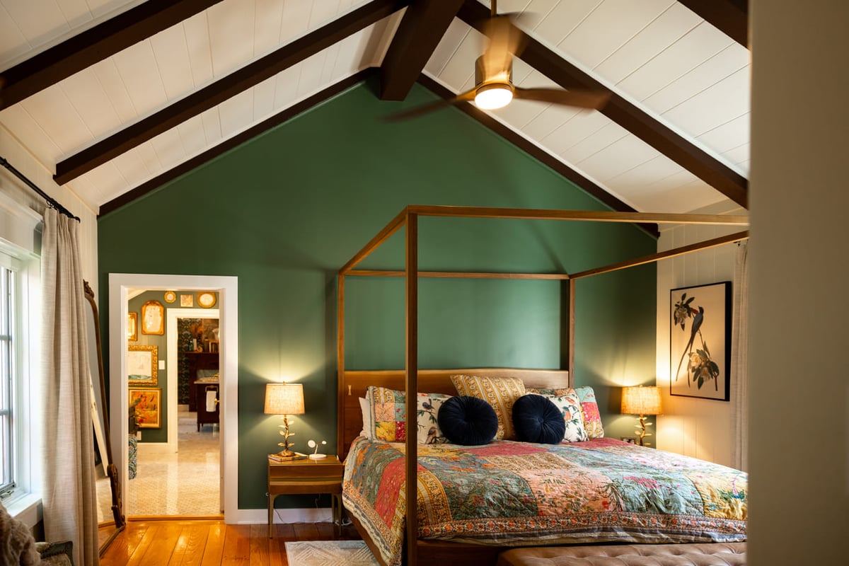Wooden canopy bed frame in bedroom with vaulted ceilings and green walls  with view into vaniety area